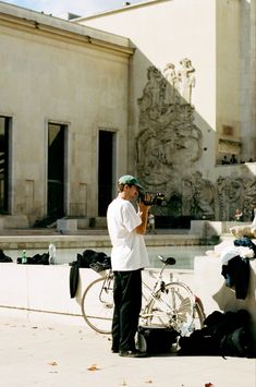 a man standing in front of a building with a bike parked next to him and another person taking a photo