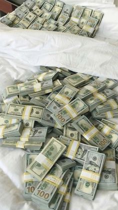 a pile of money sitting on top of a bed next to a white comforter