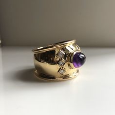 This is a beautiful statement ring. It features a vibrant purple amethyst Cabochon center stone with 6 round brilliant diamonds set in square boxes. The band is a nice thick width of 16.48mm. Amethyst is the birthstone of February. This cabochon cut Amethyst is a beautiful saturated lilac color. 1970s Vintage. Excellent condition. Metal:18k Yellow Gold. Weight: 9.47 grams Diamonds: .20ct size 9 With any pre-owned/Vintage/Antique items, it is common to have some wear, As we inspect each piece of 1970s Jewelry, Fancy Rings, Amethyst Gem, April Birthstone, Vibrant Purple, Purple Band, Large Ring, February Birthstone, Lilac Color