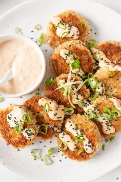 a white plate topped with crab cakes next to a small bowl of ranch dressing on the side