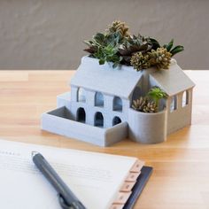 a house shaped planter sitting on top of a table next to a pen and paper