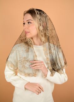 a woman wearing a veil over her head and white dress with gold embroidery on it