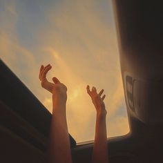 two hands reaching up into the sky from inside a vehicle with clouds in the background