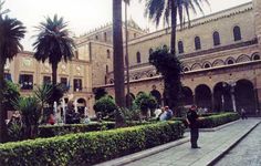 a man standing in front of a large building with palm trees on the side of it