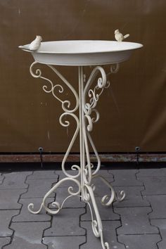 two small birds perched on top of a white birdbath with scrolled design