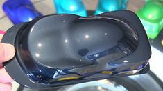 a hand holding a black heart shaped object in front of some other colorful glass objects