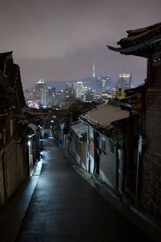 an alley way in the city at night with buildings lit up and dark skies overhead