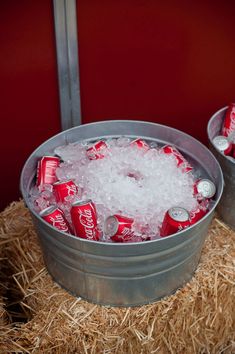 two buckets filled with ice and coca - cola are sitting on straw bales