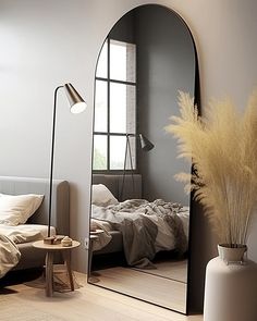 a large mirror sitting on top of a wooden floor next to a white vase filled with flowers