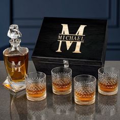 four whiskey glasses and a decanter in front of a black box on a table