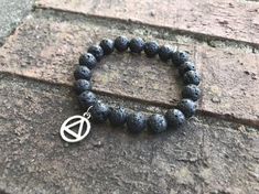 Join the Sobriety Tribe by rocking this beautiful black onyx beaded bracelet adorned with a silver AA or NA charm, which serves as a symbol of empowerment and sobriety pride!The beautiful black beads on this bracelet are the stones of sobriety and are symbolic of transformation, calmness, and clarity.  The silver circle/triangle charm is representative of recovery as this is the symbol for AA.  This beaded bracelet is on an elastic band that stretches to allow for more length.  * 8" (20cm) black Spiritual Black Beads Wristband As Gift, Spiritual Black Beaded Wristband As Gift, Black Lava Stone Stretch Bracelet As Gift, Handmade Symbolic Black Beaded Bracelets, Casual Black Jewelry For Healing, Black Lava Stone Spiritual Beaded Bracelets, Handmade Black Lava Stone Beaded Bracelets, Recovery Bracelet, Recovery Jewelry