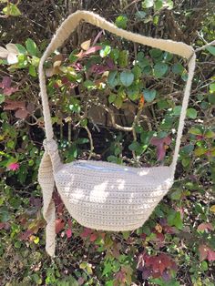 a crocheted purse hanging from a tree in front of some bushes and trees