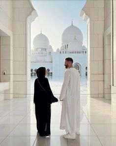 a man and woman standing in front of a large white building with arches leading into the distance