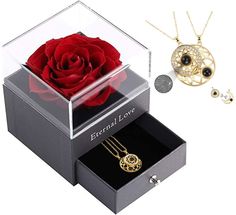 a red rose in a clear box next to a necklace and pendant on a white background