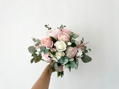 a hand holding a bouquet of flowers on a white background with greenery and leaves