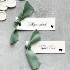 two place cards with green bows on them sitting next to some waxed seals and buttons