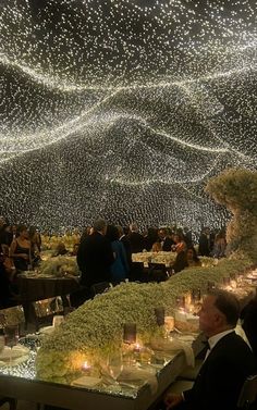 people are sitting at tables with candles and lights on the ceiling in front of them