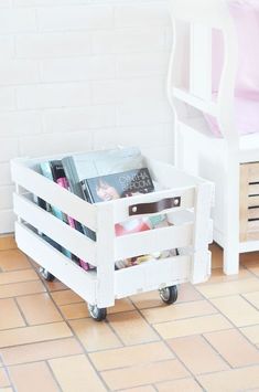 a white wooden crate filled with magazines on top of a tiled floor next to a bed