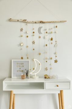 a white desk topped with a wooden branch and stars hanging from it's side