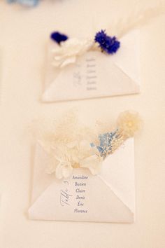 two white envelopes with blue and white flowers on them are sitting next to each other