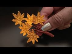 a hand holding some yellow flowers on top of a table