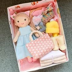 a doll and other toys in a pink box on the floor next to a window