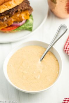 a bowl of soup next to a plate with a burger on it and a spoon in the bowl