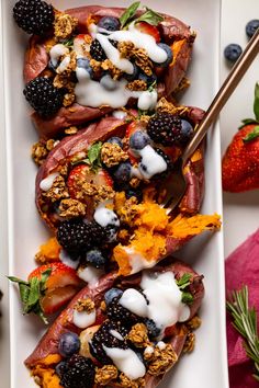 a white plate topped with meat covered in fruit and yogurt next to berries