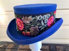 This one of a kind top hat has been hand-embellished by Immortal Kraft with stunning floral embroidered trim.  Size Medium - 57 cms. Hat body is 100% wool and fully lined.   I've had to create a new Etsy page as I've moved countries and Etsy requires me to create a new account for payment reasons .  Please see my history and ratings on my old Etsy page - ImmortalKraft Visit my new website   https://phoenixmenswear.com.au/ Lots of fun stuff for guys and girls...!! Please note that if you are ordering from anywhere outside of Australia please add your phone number as it is now required for delivery.  Thanks much. Ceremonial Blue Adjustable Hat, Adjustable Blue Ceremonial Hats, Fitted Top Hat For Winter Festivals, Winter Festival Fitted Top Hat, Traditional Fitted Blue Hat, Fitted Blue Brimmed Top Hat, Vintage Fitted Blue Hats, Fitted Top Hat For Kentucky Derby Festival, Fitted Bohemian Top Hat For Festivals