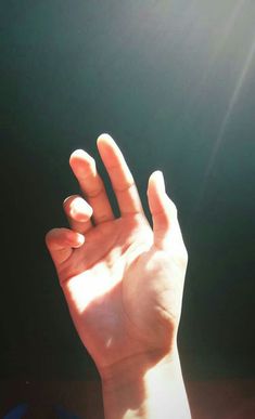 a person holding their hand up in the air with sunlight shining on them and behind them