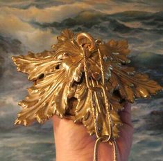 a gold leaf shaped brooch sitting on top of a persons hand in front of a painting