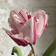 a pink flower sitting on top of a green chair next to a white brick wall