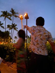 a man and woman standing next to each other under a street light with palm trees in the background