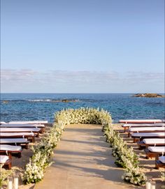 an outdoor ceremony set up with white flowers and greenery on the aisle, overlooking the ocean