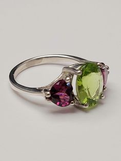 Be transported with this beautiful three stone style ring featuring a 2ct. oval cut Peridot and two Rhodolite Garnet trillion cut side stones set in sterling silver. Oval Multi-stone Peridot Gemstones, Green Three Stone Gemstones For Anniversary, 3 Stone Ring, 3 Stone Rings, Rhodolite Garnet, Three Stone, Stone Settings, Stone Ring, Houston Tx