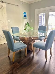 a dining room table with blue chairs and a glass top that has a tree stump on it