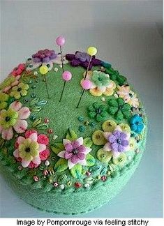 a green round box with flowers and pins on the top, sitting on a table