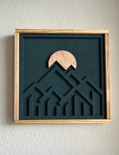 a wooden frame hanging on the wall with a paper cut out of mountains and houses