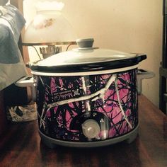 the crock pot is covered with pink and black camo print, sitting on a wooden table