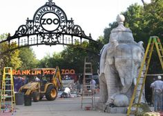 an elephant statue is under construction in front of a zoo entrance with workers working on it