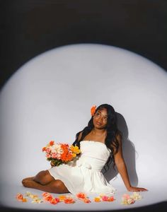 a woman in a white dress sitting on the ground with flowers all around her body