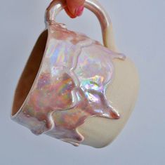 a hand holding a white vase with iridescent paint on it's side