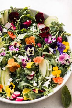 a white bowl filled with lots of different colored flowers on top of a marble table