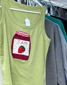 some shirts hanging up on a rack with clothes in the background and one has a jar of jam on it