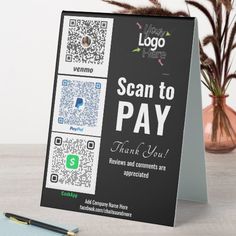 a sign that says scan to pay with qr code on it next to a pen and potted plant