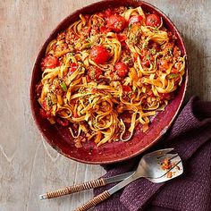 a bowl filled with pasta and meat on top of a purple cloth next to two spoons