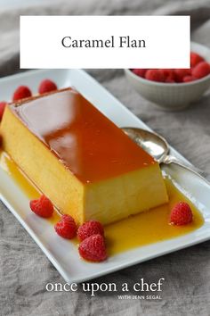 a piece of cake on a white plate with raspberries and syrup in the background