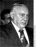 an older man in a suit and tie looking off into the distance with other people behind him