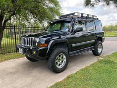 a black jeep parked on the side of a road next to a fence and trees