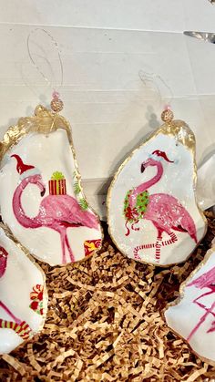 pink flamingos are painted on white ceramic ornaments in a box with wood shavings